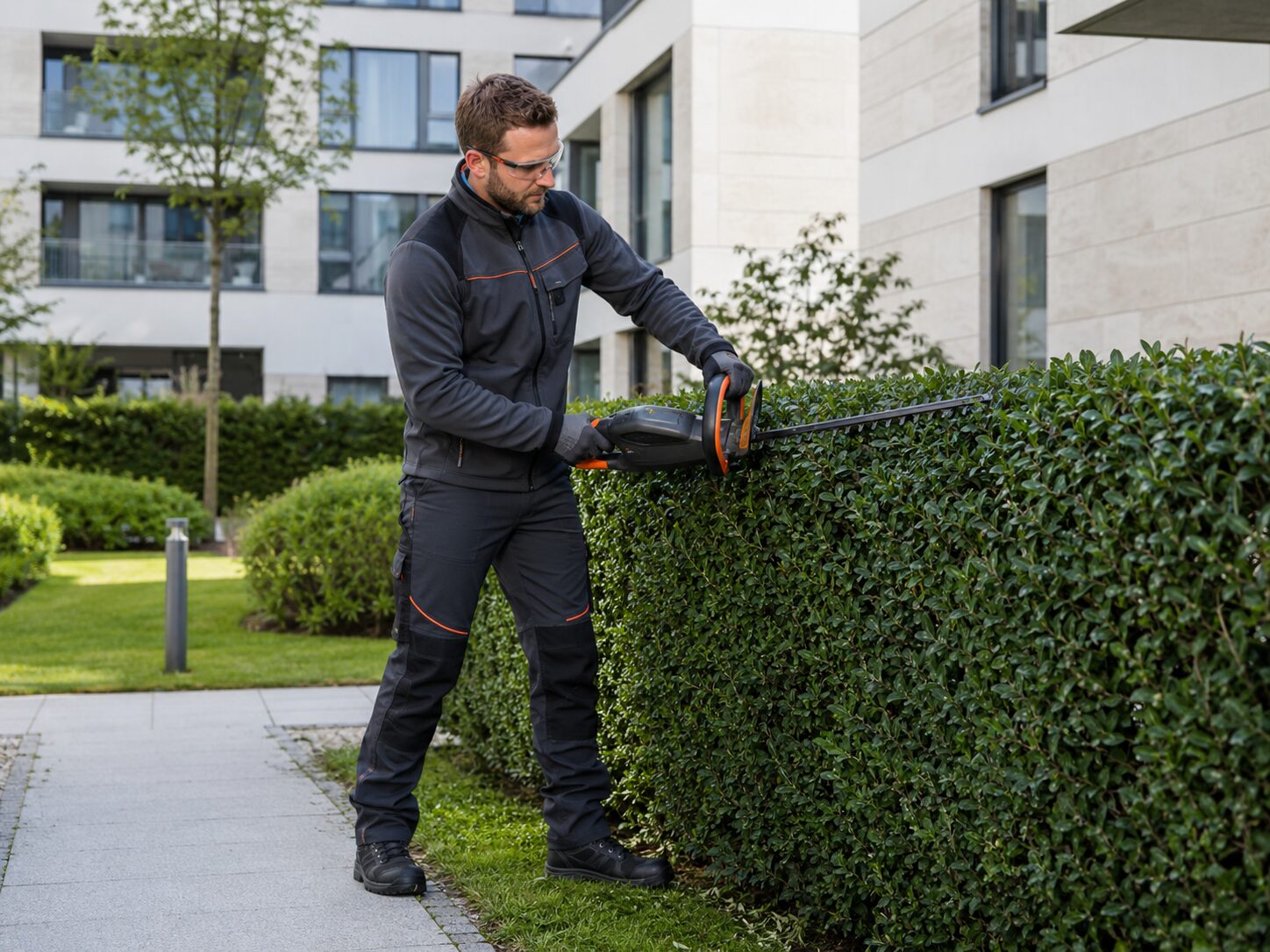 Gartenpfleger beim Heckenschnitt an einer Wohnanlage